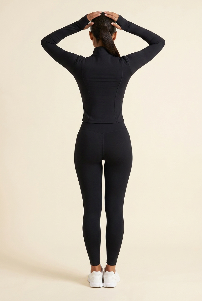 Kovelle zip through gym jacket in black, back view with hands behind her head showing the sleeves and back seams, on model