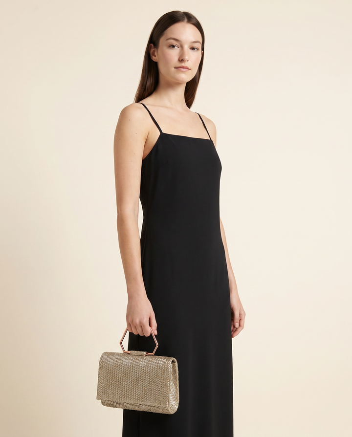 Model holding the raffia top-handle clutch with a black midi dress